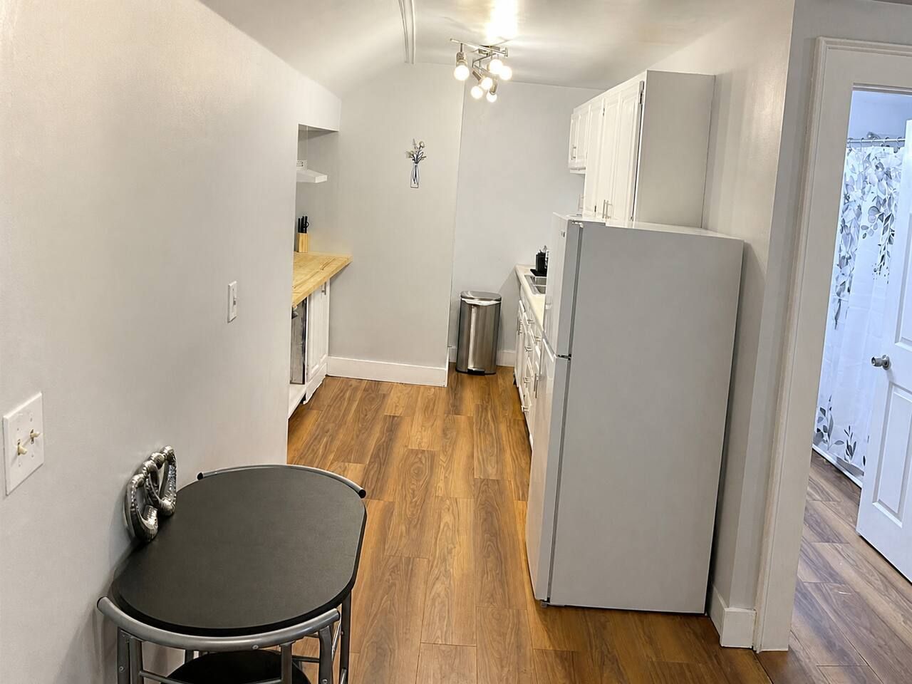 A compact kitchen with a refrigerator, a sink, and a wooden floor.