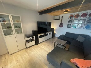 Una sala de estar moderna con televisor de pantalla plana, un sofá, una mesa de centro y un mueble con puertas de vidrio.