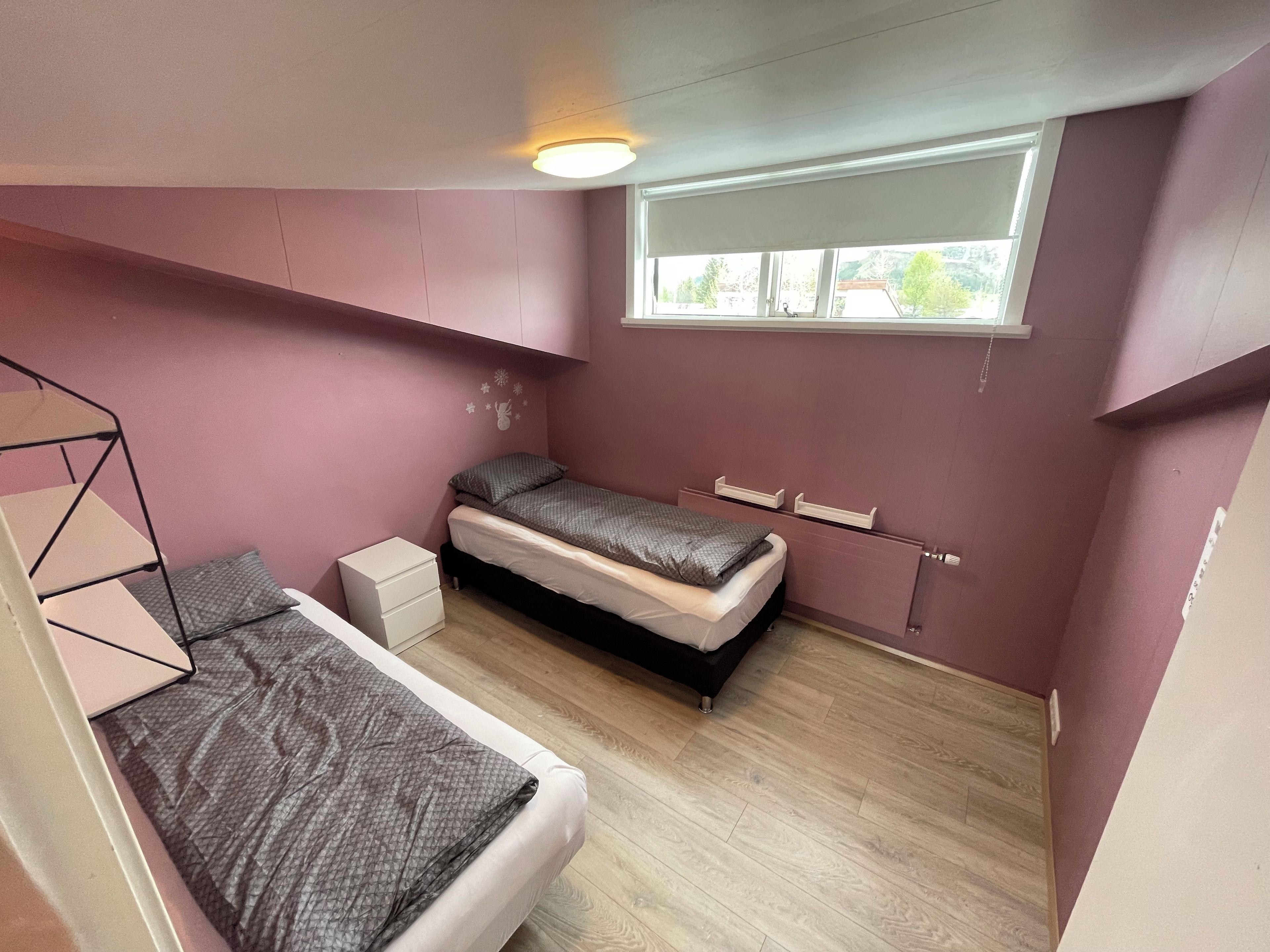 Ein Schlafzimmer mit Etagenbett, einem Einzelbett, einem Fenster mit Jalousien und einer Deckenleuchte.