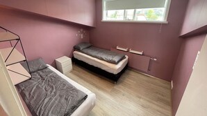 Ein Schlafzimmer mit Etagenbett, einem Einzelbett, einem Fenster mit Jalousien und einer Deckenleuchte.