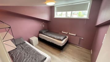 Ein Schlafzimmer mit Etagenbett, einem Einzelbett, einem Fenster mit Jalousien und einer Deckenleuchte.