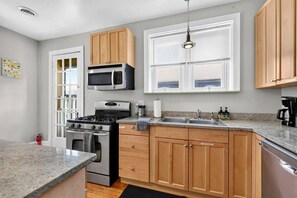 Une cuisine avec des meubles en bois, une cuisinière en acier inoxydable, un four à micro-ondes et une fenêtre avec des stores.