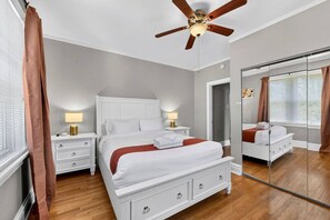 A bedroom with a bed, bedside tables, a ceiling fan, a mirror, and a sliding glass door.
