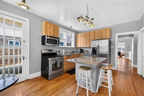 A modern kitchen with a central island, stainless steel appliances, wooden cabinets, and a bar stool seating area.