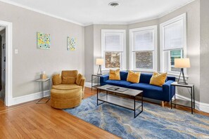 Un salon avec un canapé bleu, un fauteuil rond et deux tables d’appoint surmontées de lampes.