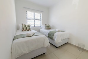 Une chambre d’hôtel avec deux lits, du linge de lit blanc et une fenêtre avec des stores.