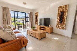 Un salon moderne avec un canapé en cuir, une table basse en bois et un téléviseur à écran plat posé sur un meuble en bois.
