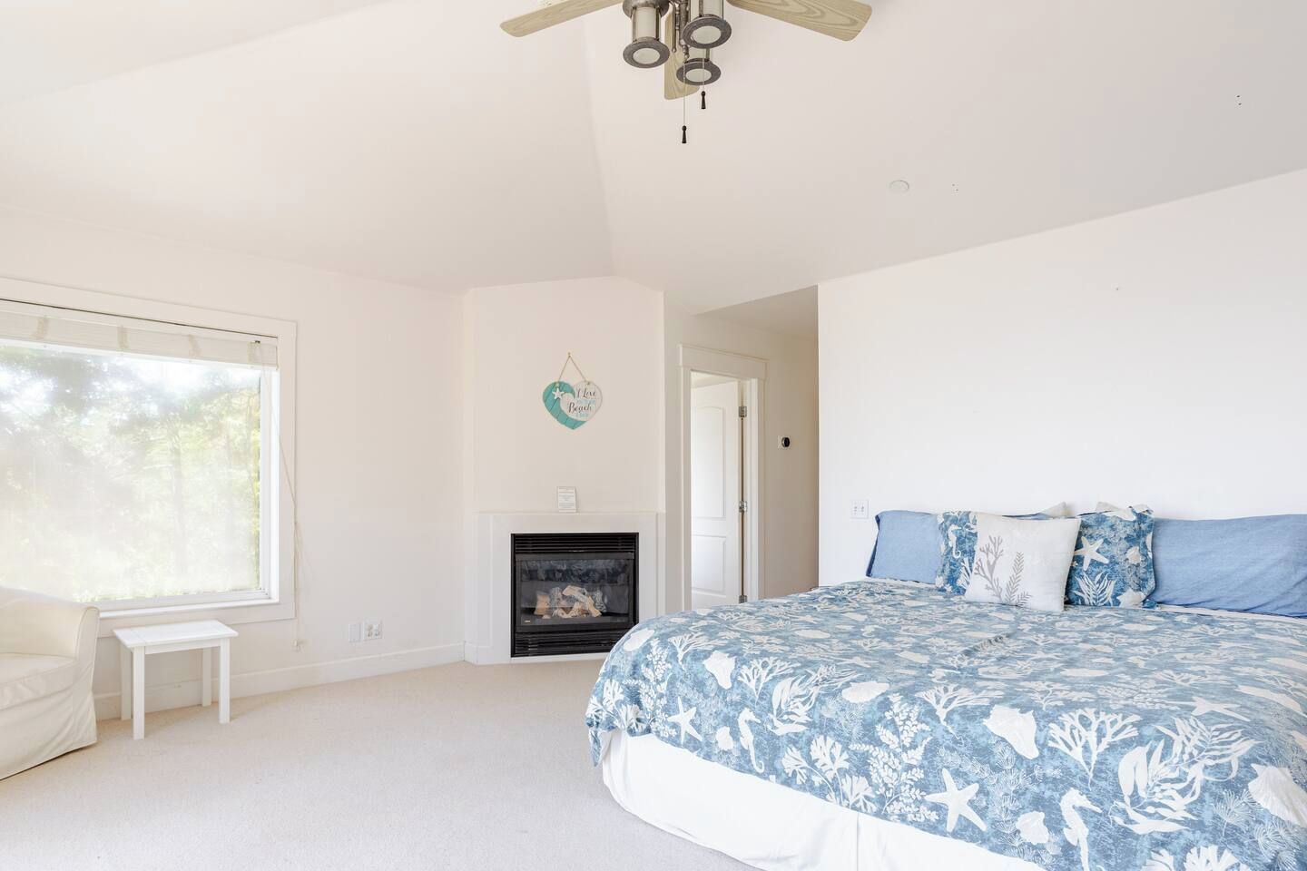 A bedroom with a bed, a fireplace, a small white bench, and a large window.