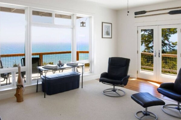 Una habitación con vista al mar, una silla negra, una mesa con un banco y un cuadro en la pared.