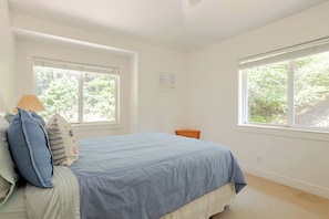 A bedroom with a bed, two windows, a nightstand, and a wall-mounted light switch.
