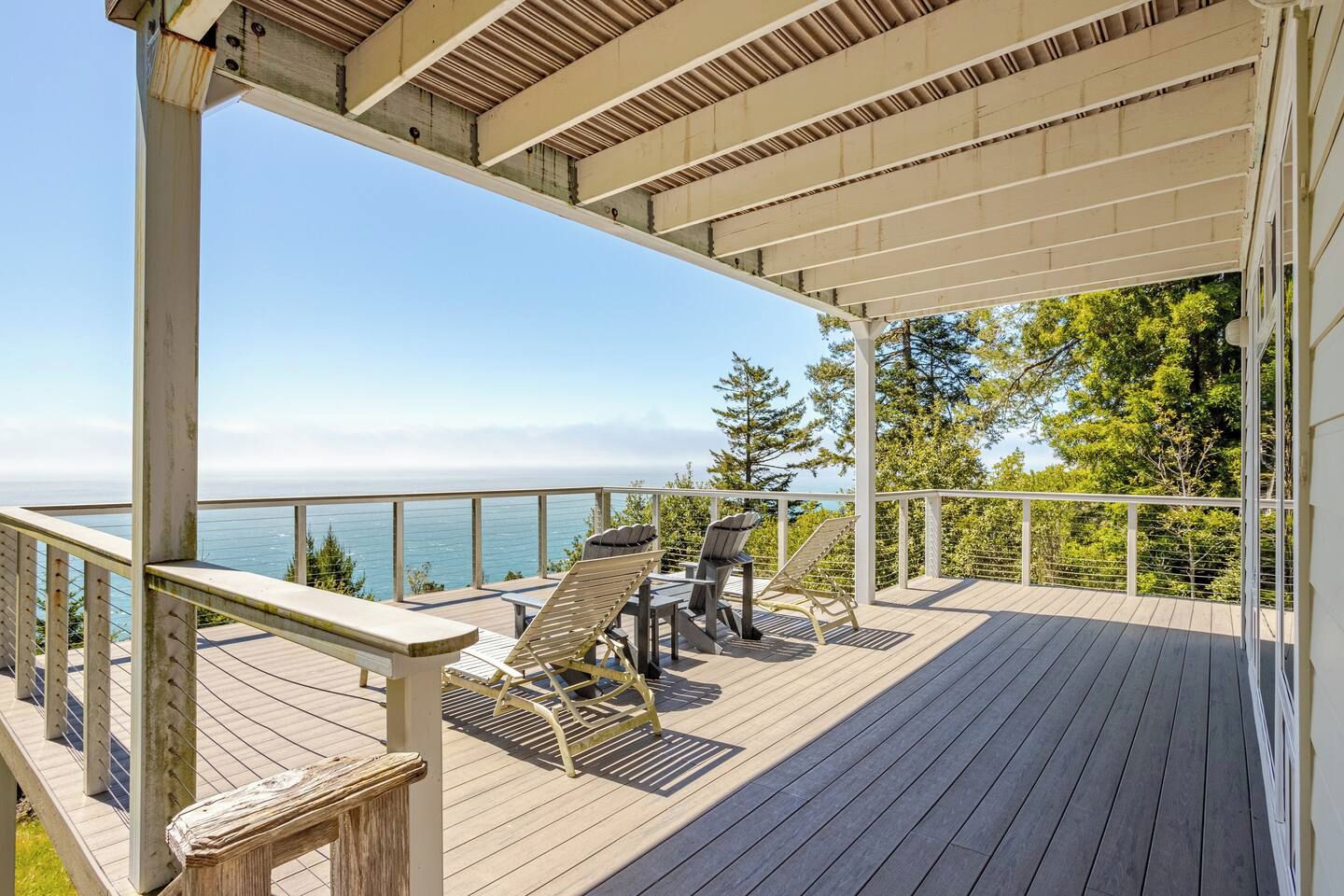 Una terraza techada con vista al océano, mobiliario de madera y barandilla.
