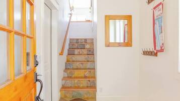 A hallway with a wooden door, a staircase with patterned tiles, a hanging pendant light, and a wall-mounted mirror.