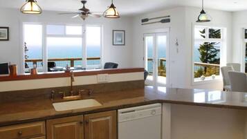 A kitchen with a view of the sea, a ceiling fan, and pendant lights.