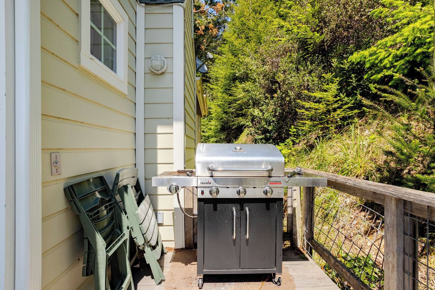 A portable grill set up on a wooden deck adjacent to a house with a window and a door.