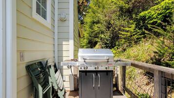 A portable grill set up on a wooden deck adjacent to a house with a window and a door.