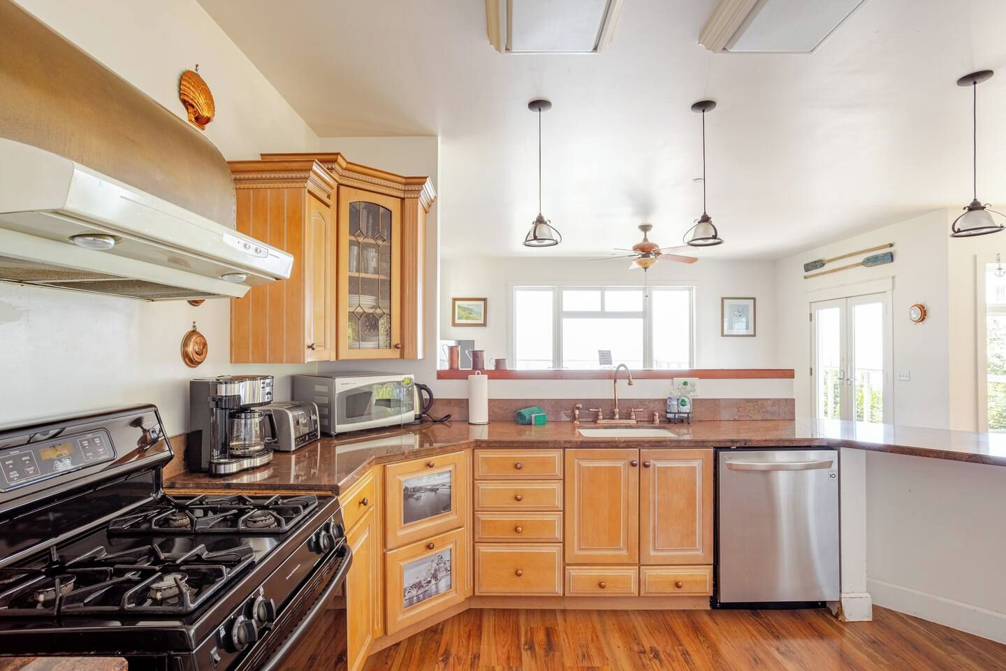 A kitchen with a stove, microwave, and coffee maker. There is a window above the sink and a ceiling fan.