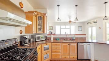A kitchen with a stove, microwave, and coffee maker. There is a window above the sink and a ceiling fan.