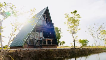 Un edificio moderno de forma triangular con fachada de vidrio, ubicado junto a una masa de agua, rodeado de árboles.