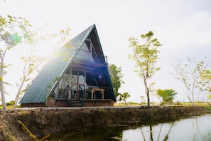 A modern, triangular-shaped building with a glass facade, situated beside a body of water, surrounded by trees. - Ruhunumaya Nature Resort (Hambantota)