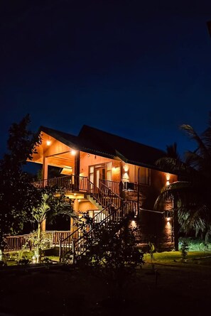 A two-story wooden building with a balcony, a staircase, and a well-lit entrance.