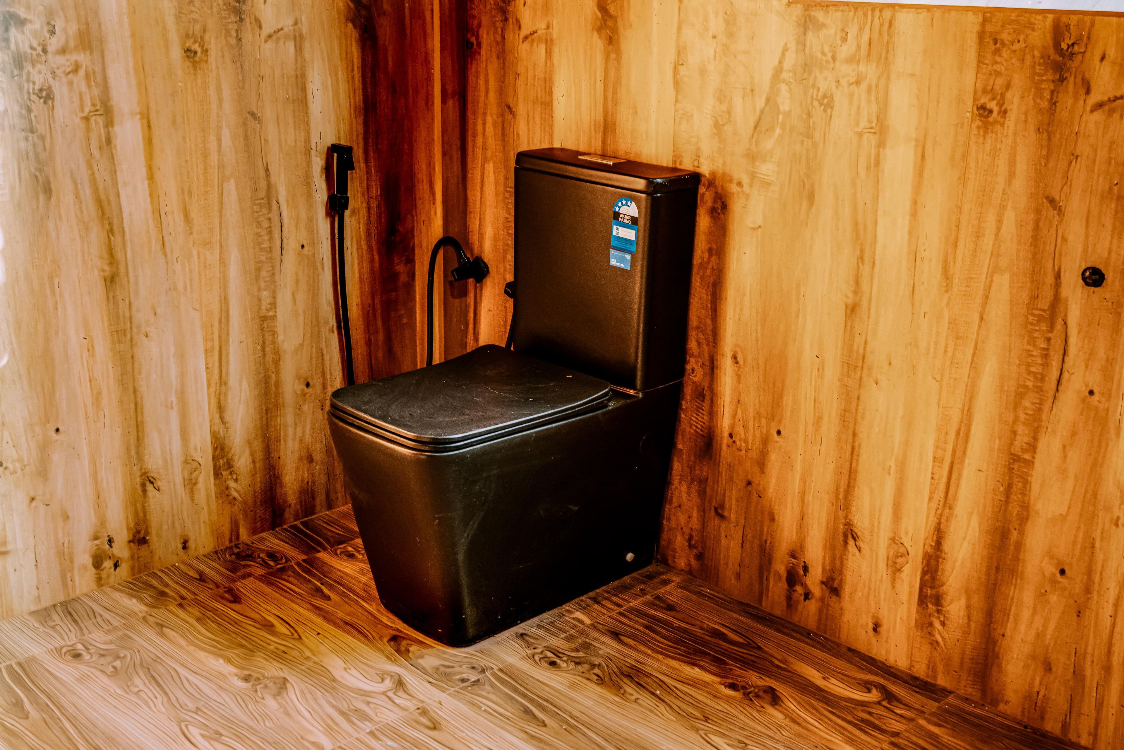 Un espacio pequeño y cerrado con interior de madera, un objeto negro pequeño con tapa y una etiqueta de contador de agua.
