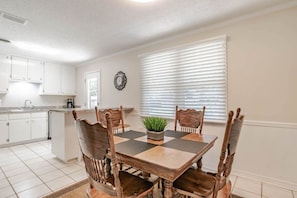A dining area with a wooden table and chairs, a potted plant, and a window with blinds. - Johnson Oaks (Mobile)