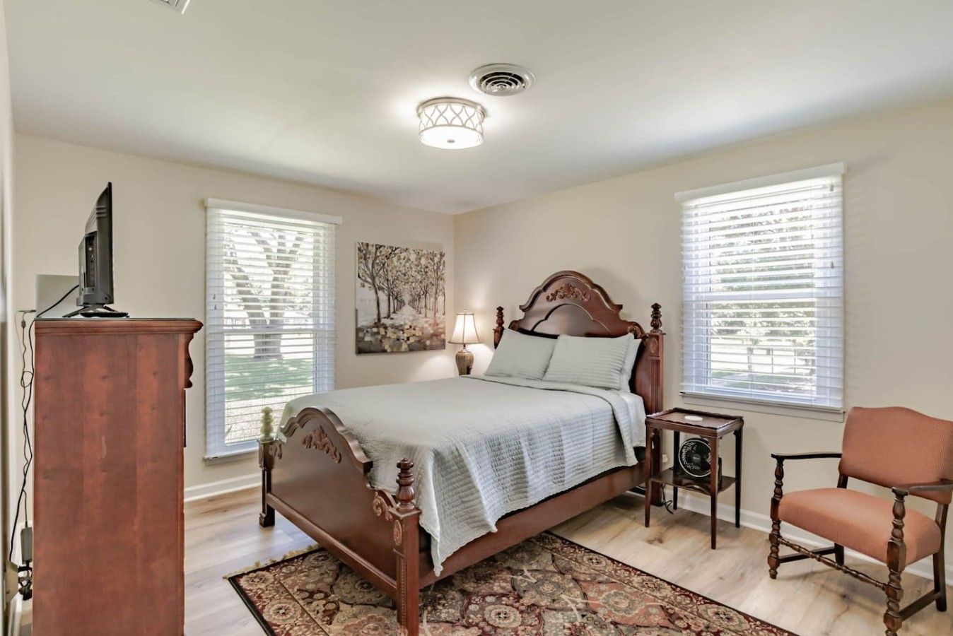 A bedroom with a wooden bed, a desk, a chair, and a small table with a lamp.