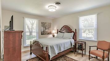 A bedroom with a wooden bed, a desk, a chair, and a small table with a lamp.