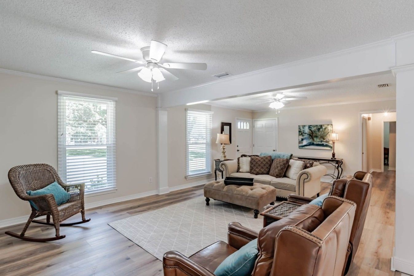 A spacious living room with a ceiling fan, a fireplace, and a large window with blinds.
