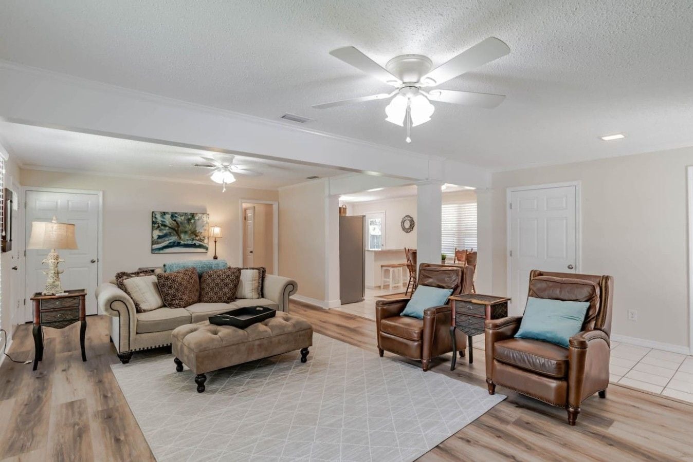A spacious living room with a ceiling fan, a sofa, two leather armchairs, and a coffee table.