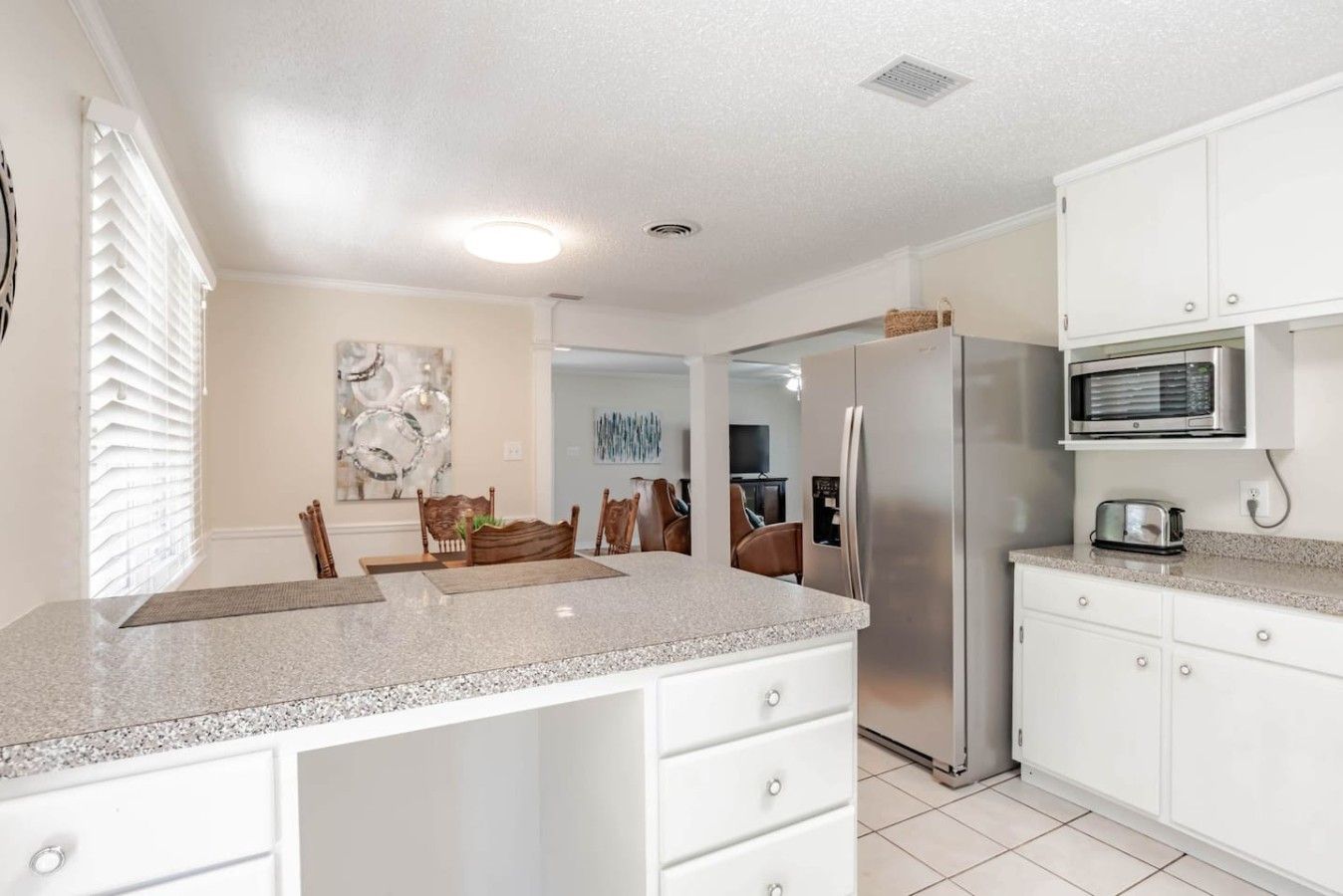 A modern kitchen with white cabinetry, a granite countertop, a stainless steel refrigerator, and a microwave.