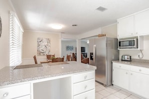 A modern kitchen with white cabinetry, a granite countertop, a stainless steel refrigerator, and a microwave. - Johnson Oaks (Mobile)