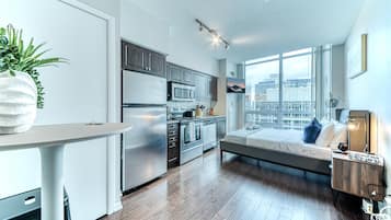 A modern apartment with a kitchen, a dining area, a bed, and a large window with a city view.