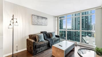 A modern living room with a sofa, a coffee table, a floor lamp, and a large window with a city view.