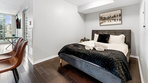 A modern hotel room with a large bed, a view of the city, and a dining area with chairs. - StayToronto - Fort York Prime Suites (Toronto)