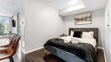 A modern hotel room with a large bed, a view of the city, and a dining area with chairs.