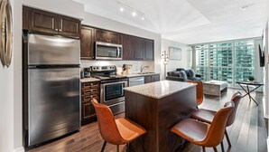 A modern kitchen with stainless steel appliances, a central island, and a dining area with chairs. - StayToronto - Fort York Prime Suites (Toronto)