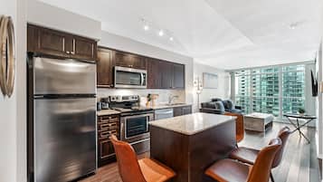 A modern kitchen with stainless steel appliances, a central island, and a dining area with chairs.