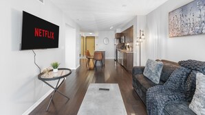 A modern living room with a flat-screen TV, a sofa, a coffee table, and a dining area in the background. - StayToronto - Fort York Prime Suites (Toronto)