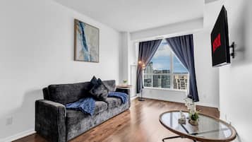 Una sala de estar moderna con un sofá gris, una mesa de centro de vidrio y un ventanal con cortinas.