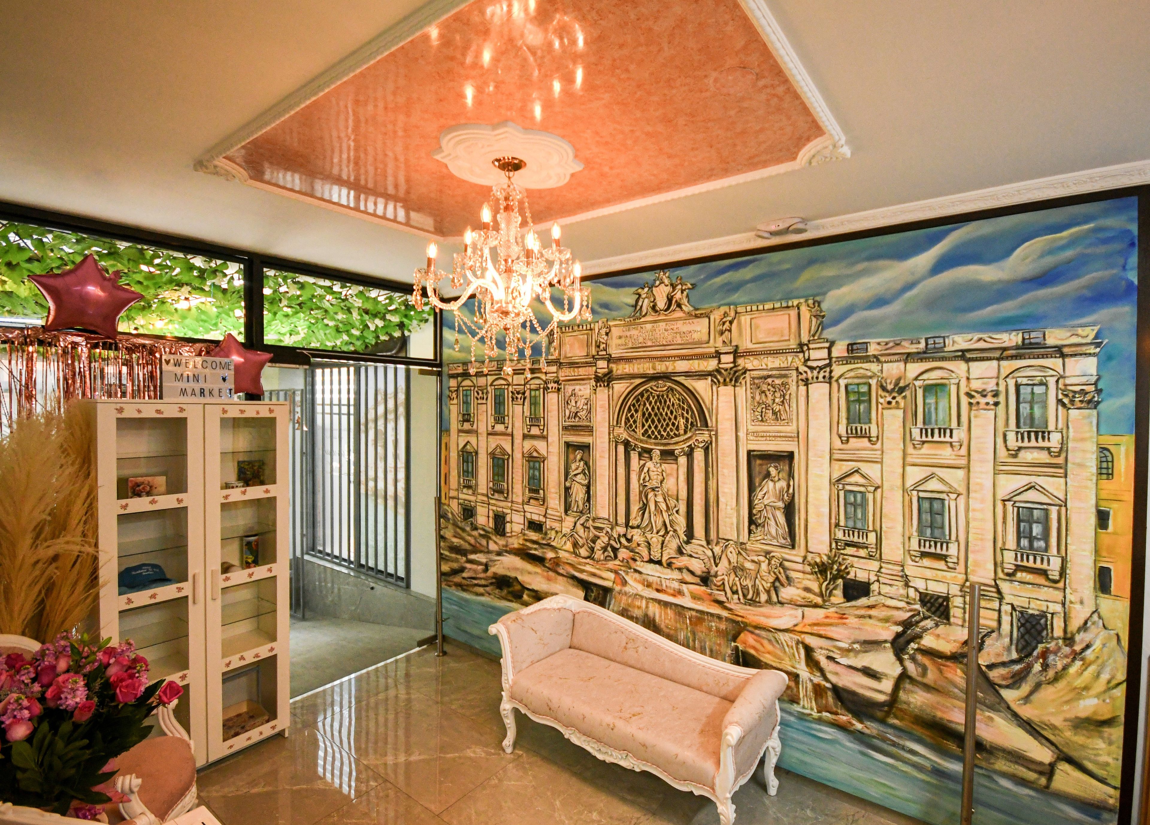 A lobby with a chandelier, a large mural of a building, a sofa, and a reception desk.