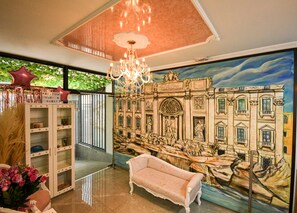 Un vestíbulo con una araña, un mural grande de un edificio, un sofá y una recepción.