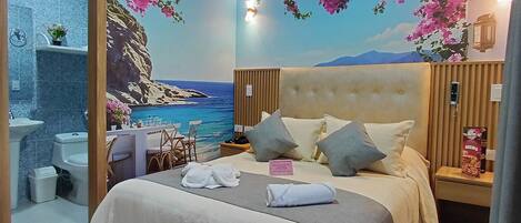 A bedroom with a bed, bedside tables, a nightstand, a bathroom with a sink, toilet, and shower, and a mural of a beach scene.