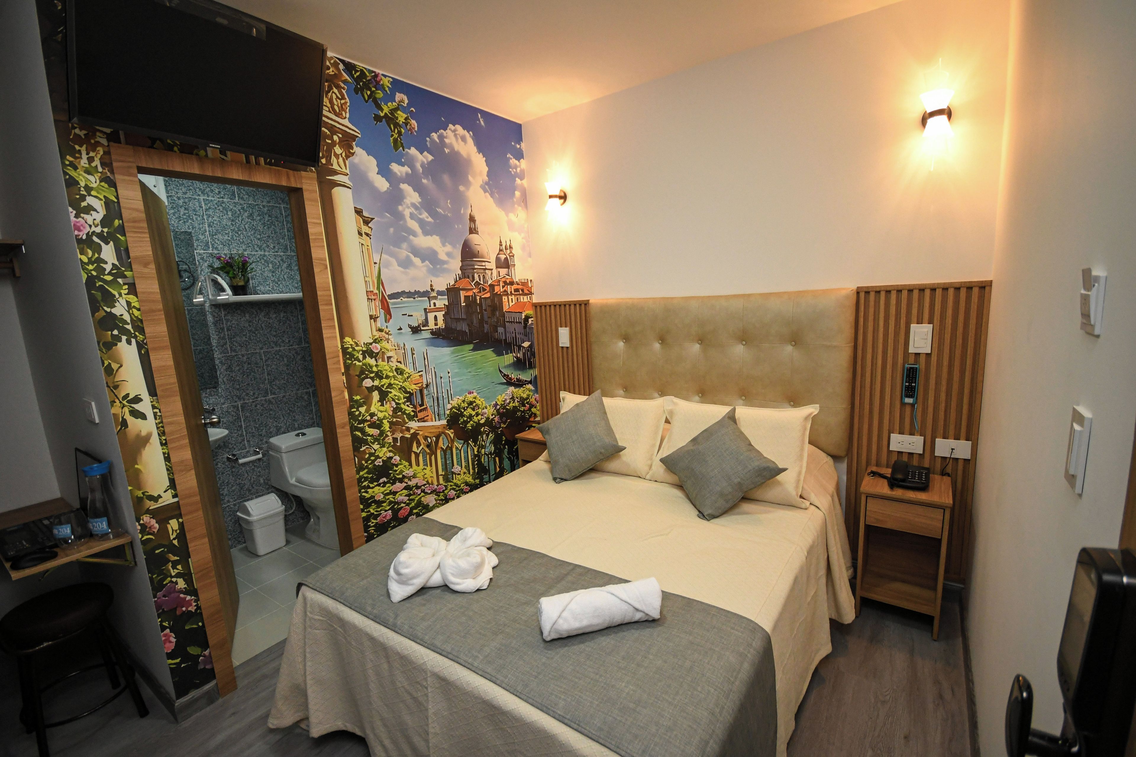 A hotel room with a bed, bedside tables, a bathroom, and a mural of a cityscape.