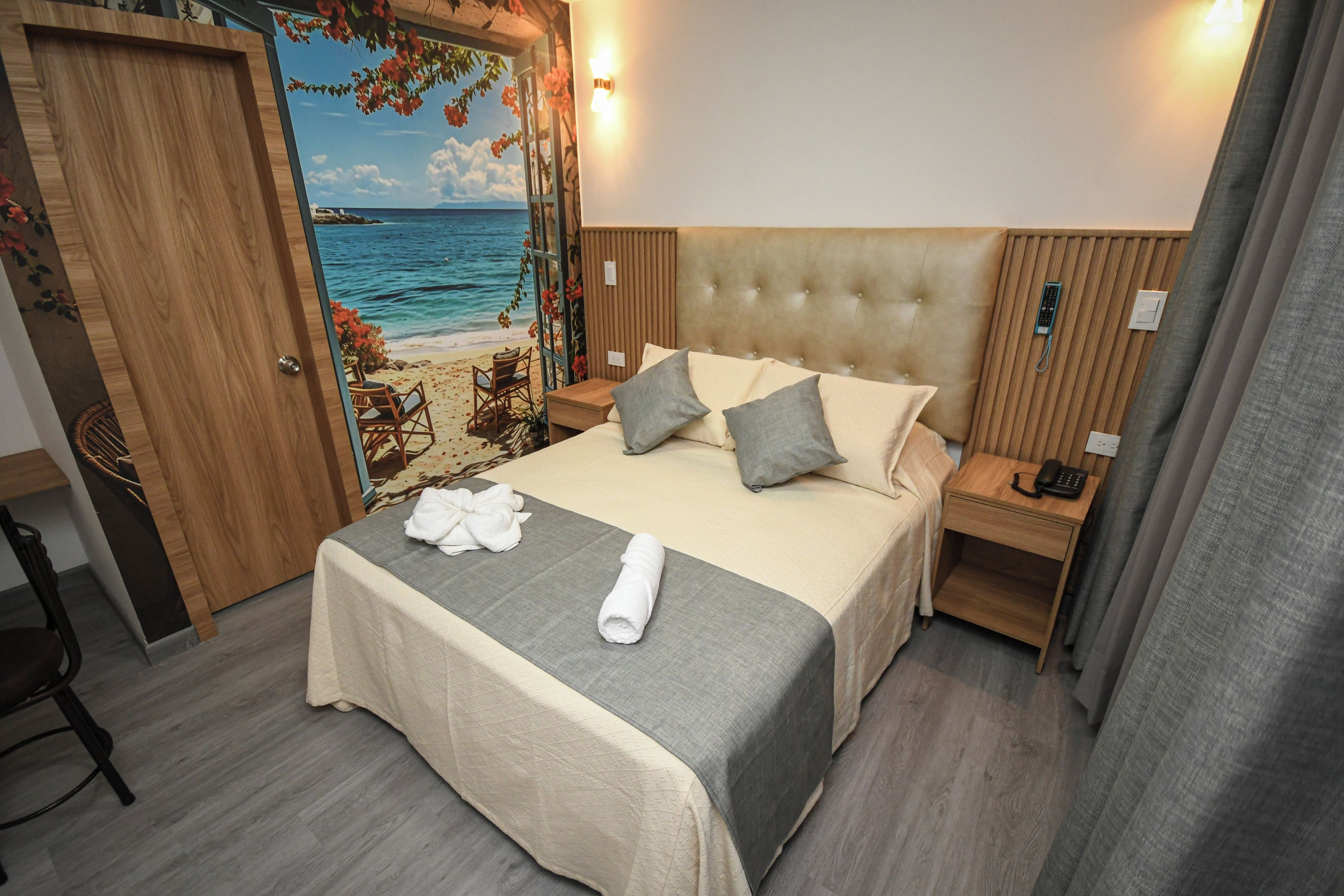 A hotel room with a bed, a nightstand, a chair, and a view of the beach through a door.