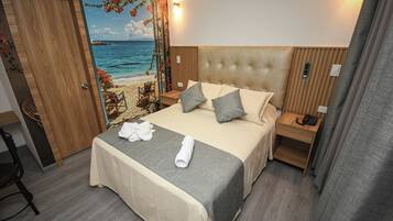A hotel room with a bed, a nightstand, a chair, and a view of the beach through a door.