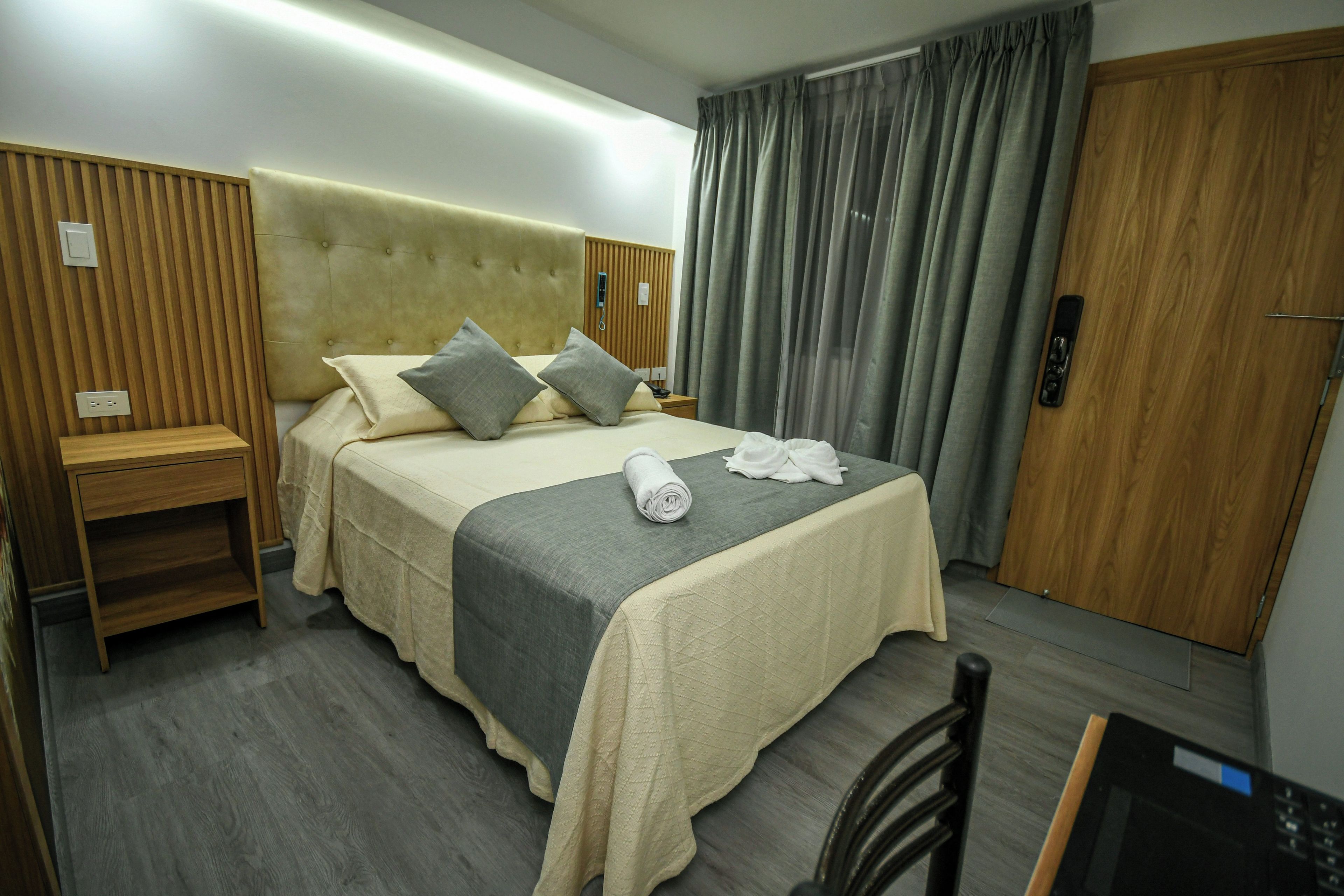 Une chambre d’hôtel comprenant un lit, des tables de chevet, un bureau, une chaise, une armoire et un rideau.