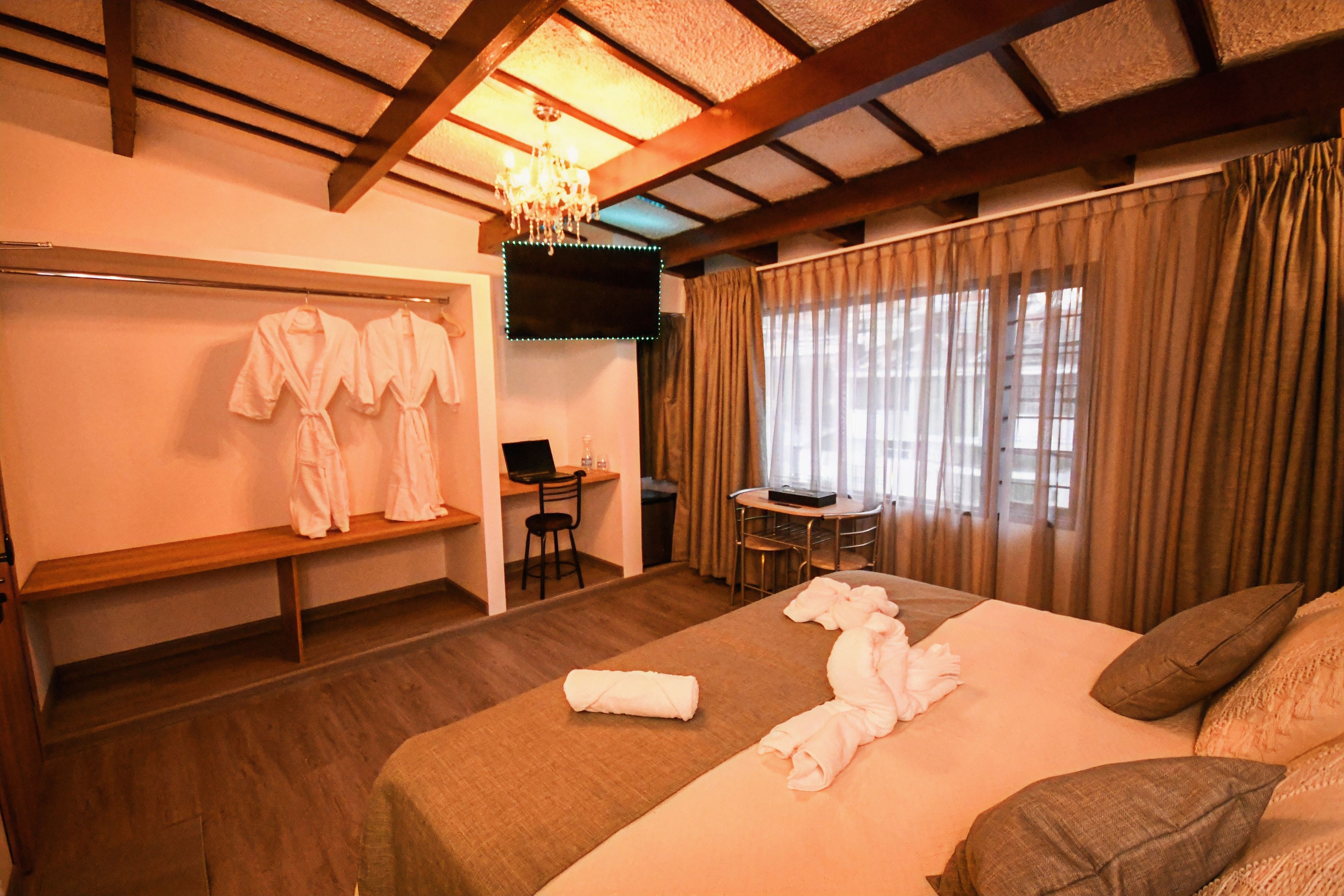 A hotel room with a bed, a desk, a chair, a TV, and a window with curtains.