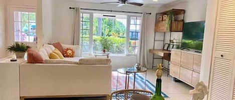 A modern living room with a sofa, dining table set with plates and cups, and a television in the background.