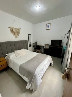 Ein Schlafzimmer mit einem Bett, einem Schreibtisch, einem Sessel, einem Fernseher und einem an der Wand befestigten Spiegel.